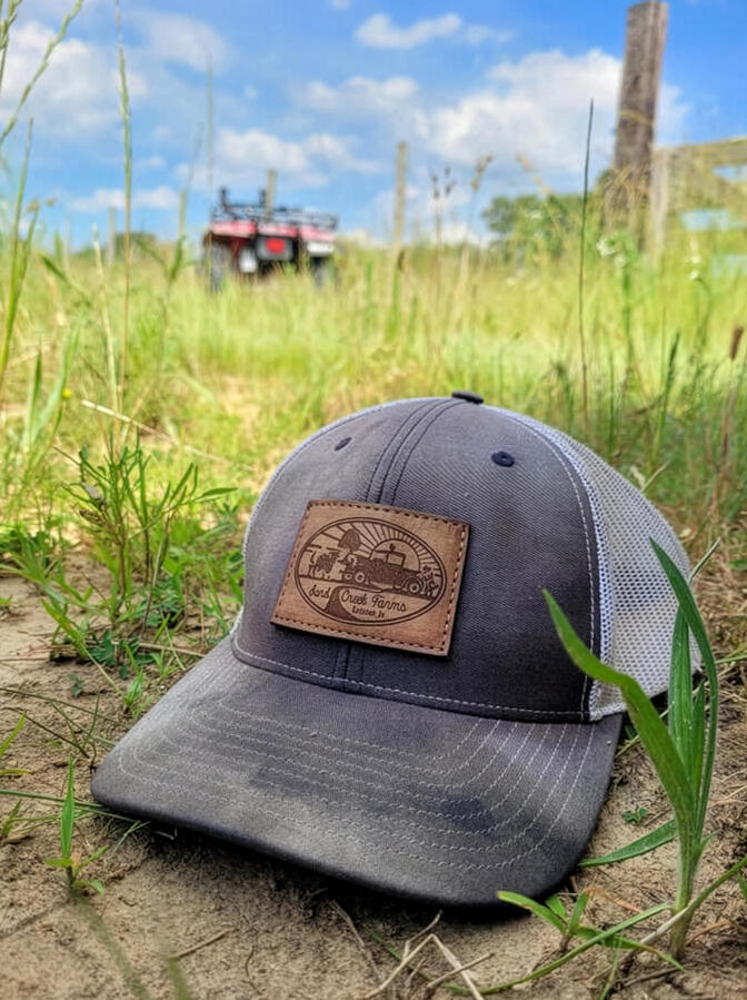 Sand Creek Farms logo applied to a leather patch on a trucker hat, photographed on the farm.